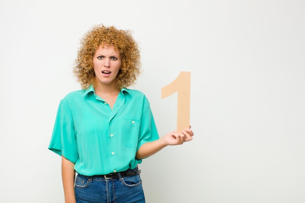 Jovem mulher bonita afro confusa, duvidosa, pensando, segurando um número 1.