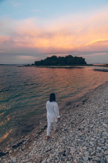 Jovem mulher bonita andando na praia olhando o pôr do sol acima do mar