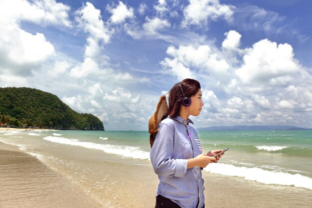 jovem mulher bonita andando na praia ouvindo música em fones de ouvido