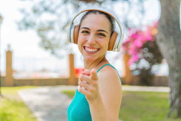 Jovem mulher bonita ao ar livre ouvindo música e apontando para a frente