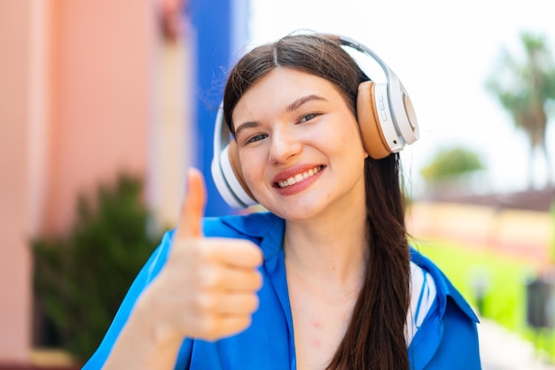 Jovem mulher bonita ao ar livre ouvindo música e com o polegar para cima