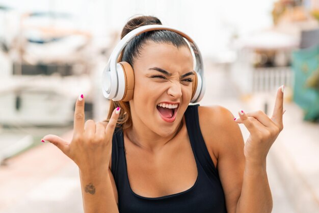 Foto jovem mulher bonita ao ar livre ouvindo música fazendo gesto de rock