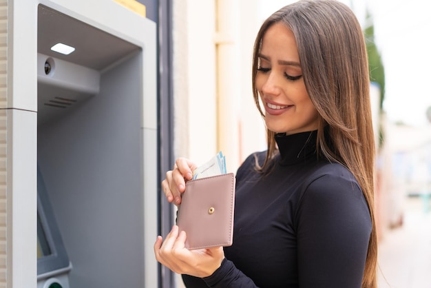 Jovem mulher bonita ao ar livre usando um caixa eletrônico