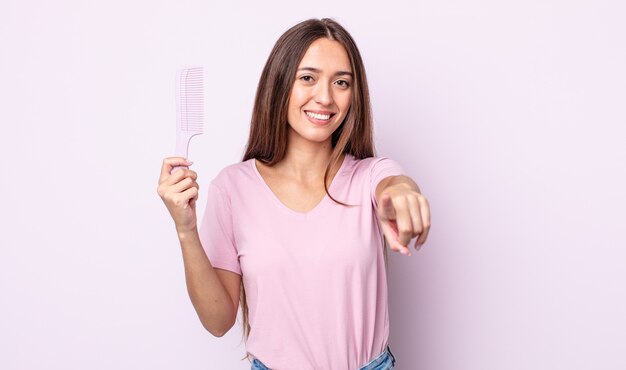 Jovem mulher bonita apontando para a câmera escolhendo você. conceito de pente de cabelo