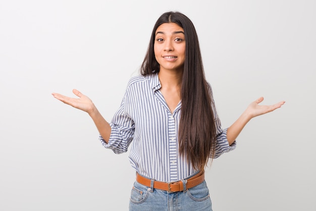 Jovem mulher bonita árabe confusa e duvidosa encolher os ombros os ombros para manter um espaço de cópia.