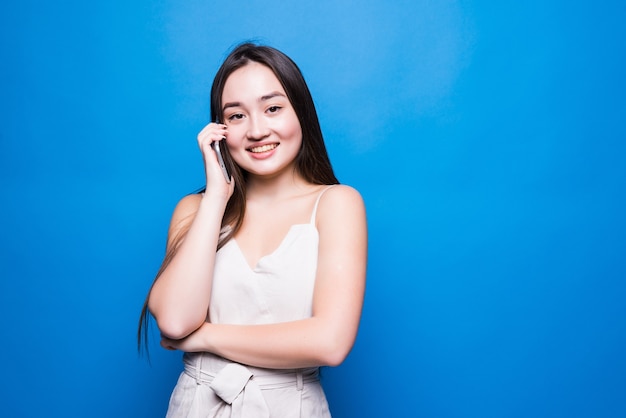 Jovem mulher bonita asiática falando no celular, isolada sobre a parede azul