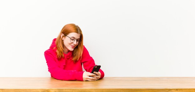 Jovem mulher bonita cabeça vermelha na frente de uma mesa de madeira com um telefone móvel