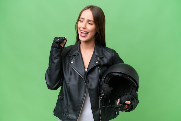 Jovem mulher bonita caucasiana com um capacete de moto sobre fundo isolado comemorando uma vitória