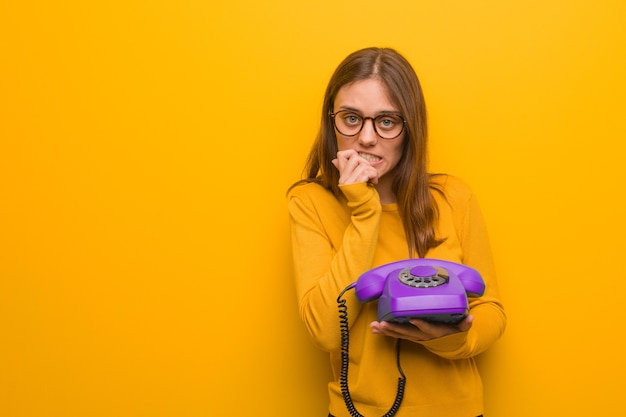 Jovem mulher bonita caucasiana roendo as unhas, nervosa e muito ansiosa. ela está segurando um telefone vintage.