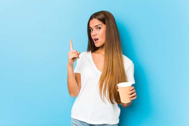 Jovem mulher bonita caucasiana segurando um café para viagem, tendo uma ideia, o conceito de inspiração.