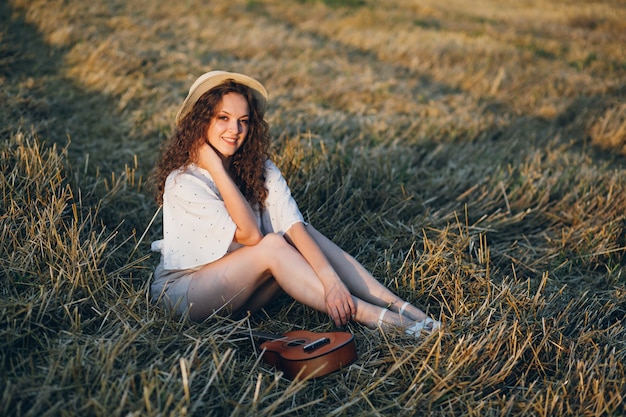 Jovem mulher bonita com cabelo longo encaracolado posa num campo de trigo no verão ao pôr do sol