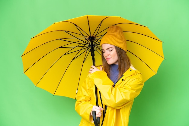 Jovem mulher bonita com casaco à prova de chuva e guarda-chuva sobre fundo croma chave isolado, sofrendo de dor no ombro por ter feito um esforço