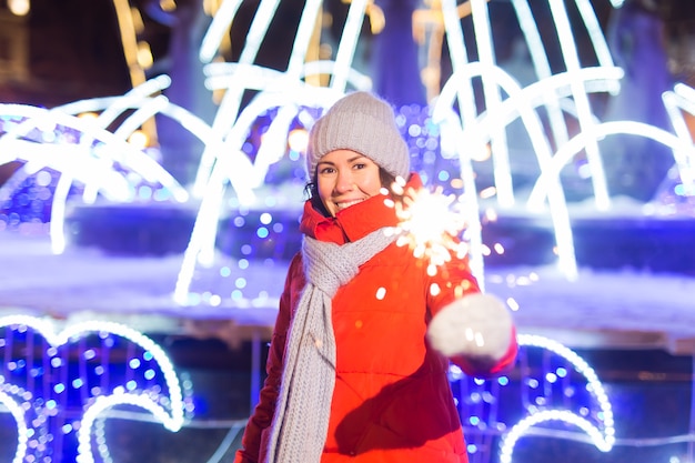 Jovem mulher bonita com chapéu de malha e lenço em pé na cidade com luz de Bengala, diamante. Celebração do conceito e Natal.