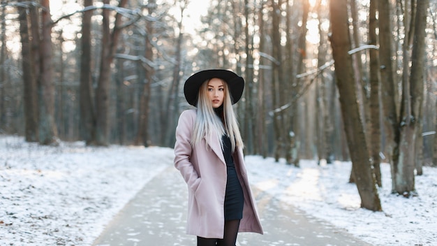 Jovem mulher bonita com chapéu elegante na moda e casaco em pé em um parque de inverno