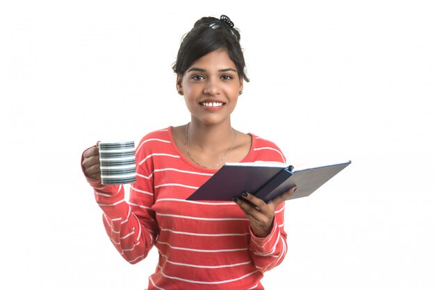 Jovem mulher bonita com livro e xícara de café que levanta em uma parede branca.