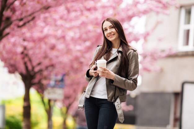 Jovem mulher bonita com longos cabelos escuros aprecia a beleza da natureza primavera perto da árvore de sakura