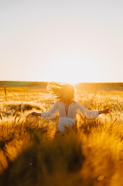 jovem mulher bonita com longos cabelos loiros em um vestido branco em um campo de trigo no início da manhã ao nascer do sol. O verão é a hora dos sonhadores, cabelos voadores, uma mulher correndo pelo campo nos raios