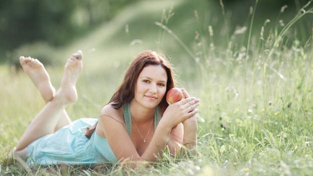 Jovem mulher bonita com maçã descansando na grama verde fresca. Foto com espaço de cópia