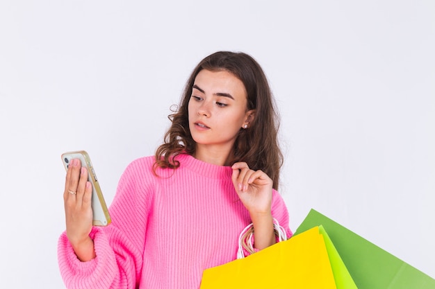 Jovem mulher bonita com maquiagem leve sardas em suéter na parede branca com sacolas de compras e telefone celular