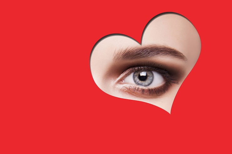 Foto jovem mulher bonita com maquiagem olhos esfumaçados, olhando para a câmera através da forma de coração vermelho. estúdio interno tiro isolado sobre fundo vermelho.