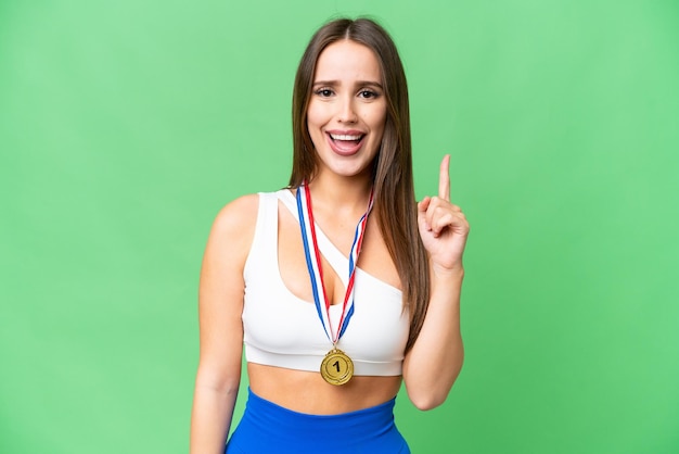 Jovem mulher bonita com medalhas sobre fundo croma chave isolado apontando para cima uma ótima ideia