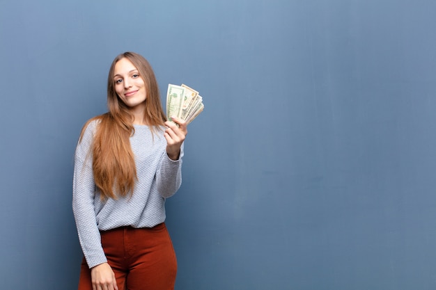 Jovem mulher bonita com notas de dólar contra a parede azul com um espaço de cópia