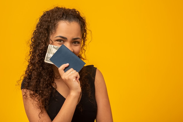 Foto jovem mulher bonita com o cabelo encaracolado que guarda um passaporte e dinheiro, pensando de sua viagem seguinte.