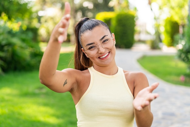 Foto jovem mulher bonita com óculos ao ar livre apresentando e convidando para vir com a mão