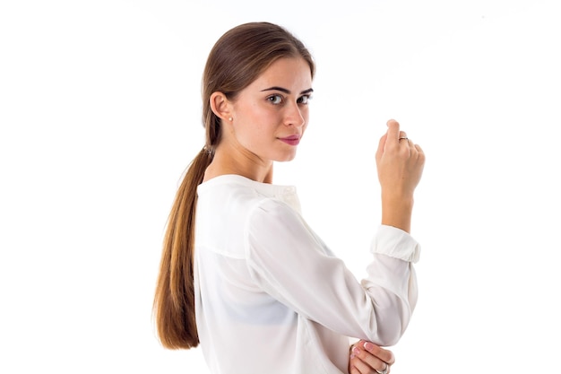 Jovem mulher bonita com rabo de cavalo vestindo uma blusa branca sobre fundo branco no estúdio