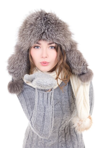 Jovem mulher bonita com roupas de inverno soprando algo com as palmas das mãos isoladas no fundo branco