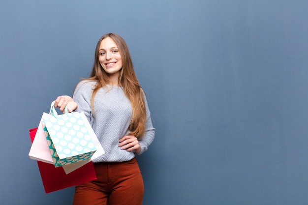 Jovem mulher bonita com sacos de compras contra a parede azul com um copyspace