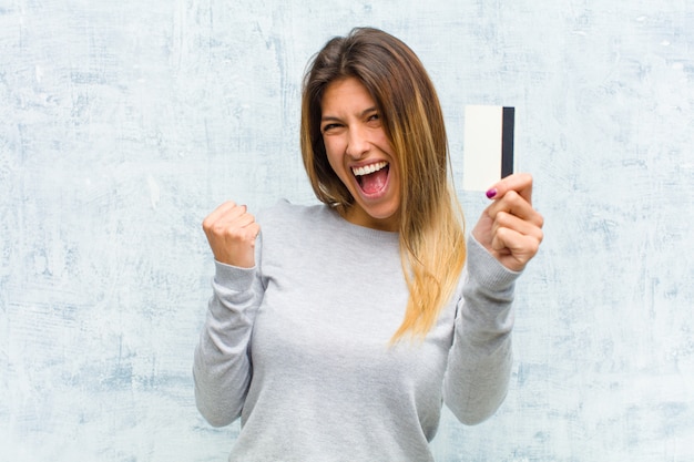 Jovem mulher bonita com um cartão de crédito contra a parede do grunge