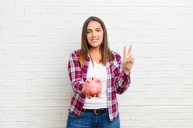 Jovem mulher bonita com um cofrinho contra a textura da parede de tijolo