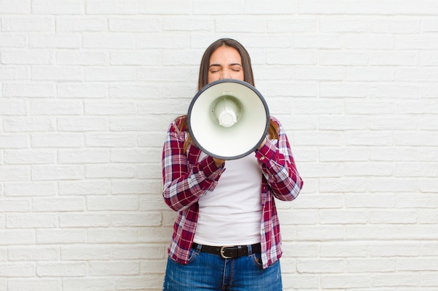 Jovem mulher bonita com um megafone contra a textura da parede de tijolo