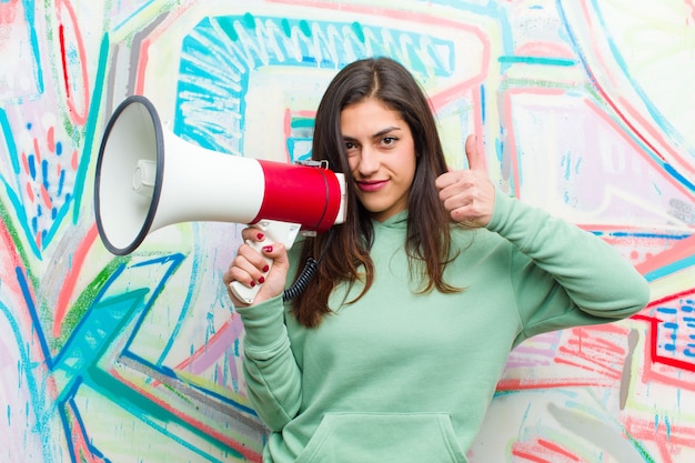 Jovem mulher bonita com um megafone contra parede grafite