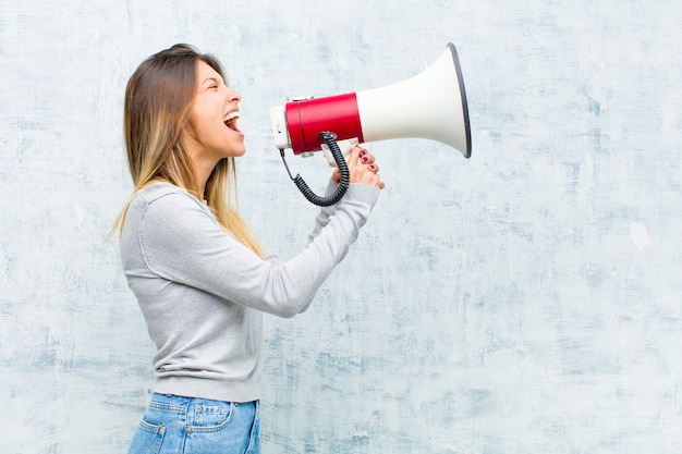 Jovem mulher bonita com um megafone contra parede grunge