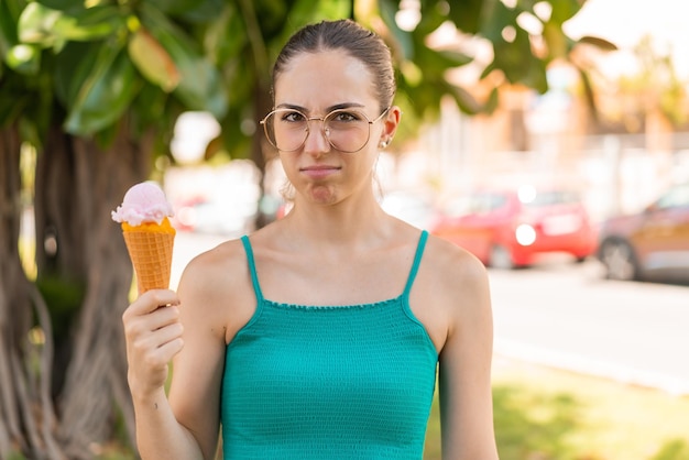 Jovem mulher bonita com um sorvete de corneta ao ar livre com expressão triste