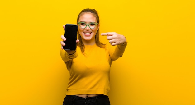 Jovem mulher bonita com um telefone inteligente contra fundo amarelo