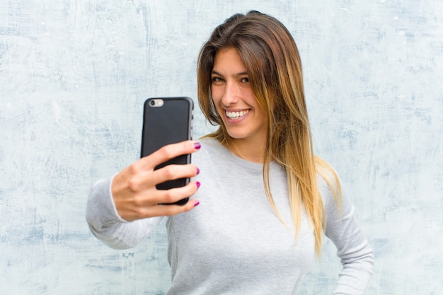 Jovem mulher bonita com um telefone inteligente contra parede grunge