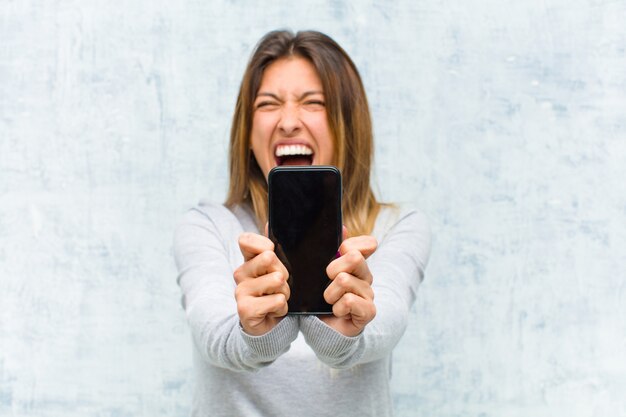 Jovem mulher bonita com um telefone inteligente contra parede grunge