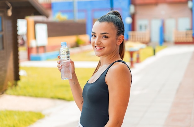 Jovem mulher bonita com uma garrafa de água ao ar livre, sorrindo muito