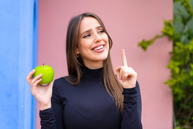 Jovem mulher bonita com uma maçã ao ar livre com a intenção de perceber a solução enquanto levanta um dedo