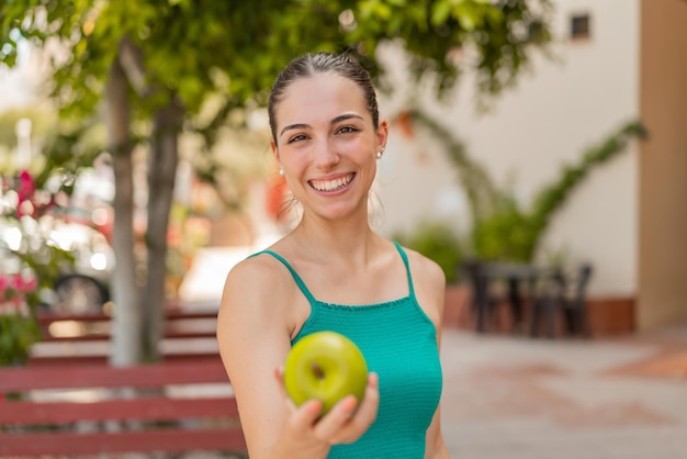 Jovem mulher bonita com uma maçã ao ar livre com expressão feliz