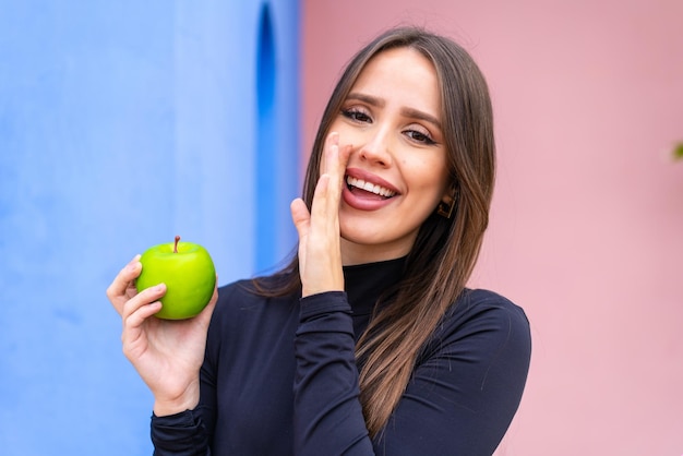 Jovem mulher bonita com uma maçã ao ar livre sussurrando algo