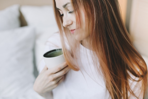Jovem mulher bonita com uma xícara de café na cama em casa