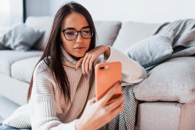 Jovem mulher bonita de óculos sentado em casa sozinho com o telefone nas mãos.