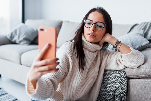 Jovem mulher bonita de óculos sentado em casa sozinho com o telefone nas mãos.