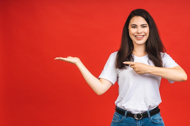 Jovem mulher bonita de pé isolada sobre fundo vermelho sorrindo mostrando as duas mãos abertas as palmas das mãos apresentando e comparação e equilíbrio de publicidade