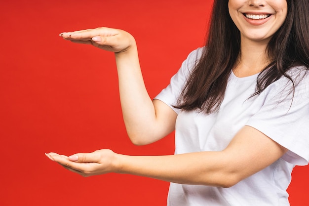 Jovem mulher bonita de pé isolada sobre fundo vermelho sorrindo mostrando as duas mãos abertas as palmas das mãos apresentando e comparação e equilíbrio de publicidade