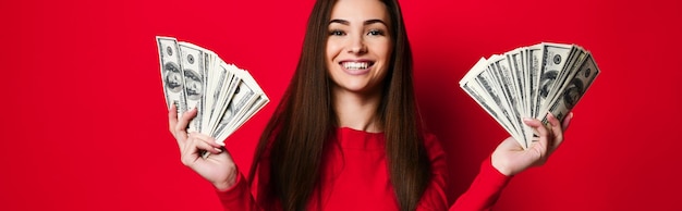 Jovem mulher bonita de vestido vermelho se escondendo atrás de um monte de notas de dinheiro